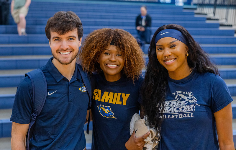 Three alum standing in front of bleachers in a gym.
