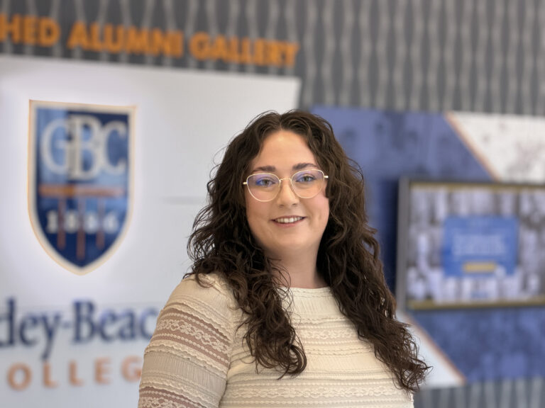 Amanda Berthiaume, Assistant Director of Undergraduate Admissions at Goldey-Beacom College poses in front of the alumni gallery in GBC's event center