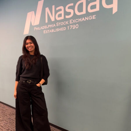 GBC student, Kiran Matro, in front of the Nasdaq logo.