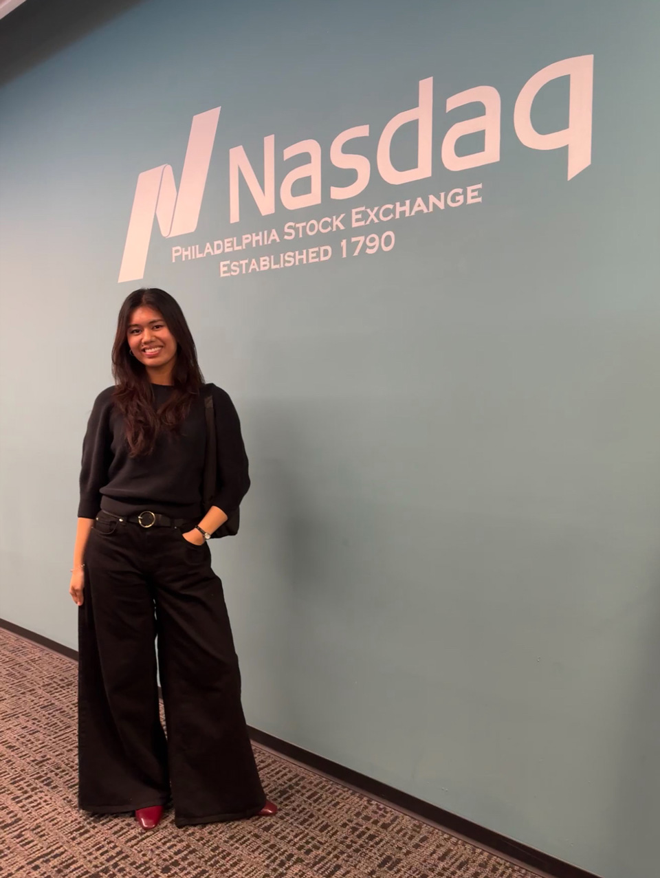 GBC student, Kiran Matro, in front of the Nasdaq logo.