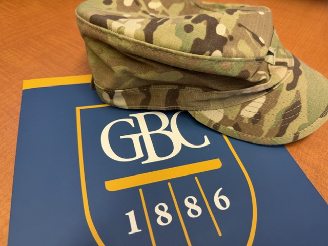GBC acceptance folder on a table with a military camouflage hat placed on the top corner of the folder.