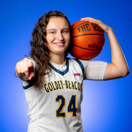Azra Ozgul, GBC student athlete, holding a basketball and pointing at the camera in front of a blue background.