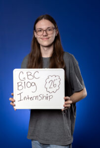 Chase Mulligan poses with a whiteboard with the words "GBC Blog Micro-internship '26"