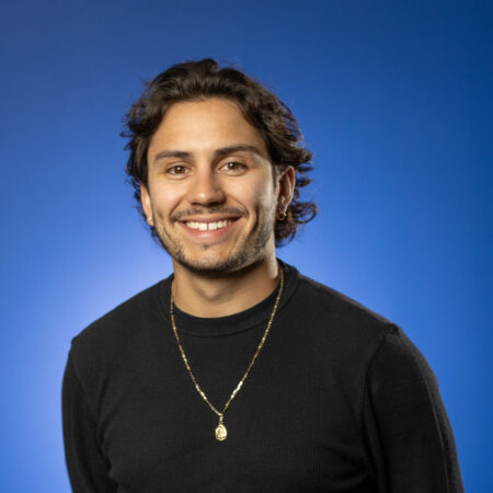 JJ Becerra poses for a headshot in GBC's Lightning Studio against a bright blue backdrop