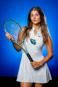 GBC student athlete and tennis player, Macy Hendin-Walker, posing with a tennis racket in front of a blue background