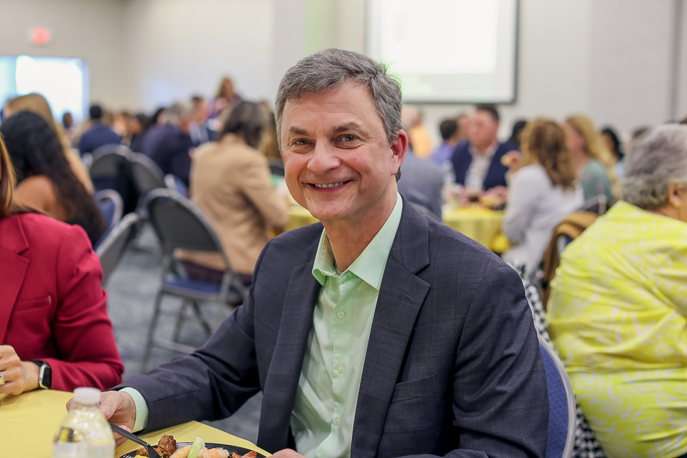 Founders Circle member, Mark Olazagasti sitting at a GBC event with people in the background.